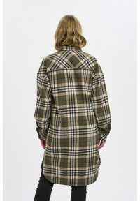 Veste chemise à carreaux verts avec manches longues, dotée d'une fermeture à boutons et d'un ourlet arrondi. Le tissu est texturé et chaud.