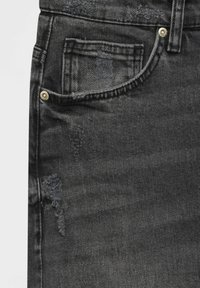 Jeans de mezclilla negra con un aspecto desgastado, bordes deshilachados, un diseño clásico de cinco bolsillos y acentos de hardware en tono dorado.