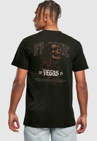 Juodas medvilnės marškinėliai su skeletų grafika ir tekstais "FLAME" bei "VEGAS 2025" kontrastingomis spalvomis ant nugaros. Trumpomis rankovėmis.