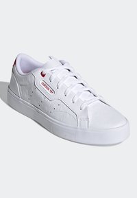 Vita Adidas-sneakers med texturerade blommönster, snörning och röda accenter. Utrustade med en vadderad krage och rundad tådesign.