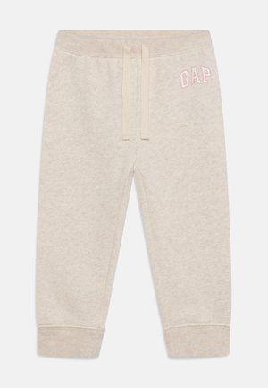Svetlo béžové jogger nohavice z mäkkej látky, s elastickým pásom so šnúrkou, rebrovanými manžetami a logom "GAP" v ružovej farbe na ľavej strane.
