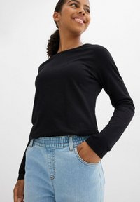 Maglietta nera a maniche lunghe abbinata a jeans in denim blu chiaro con vita elastica e tasche laterali. Tessuto morbido con vestibilità rilassata.