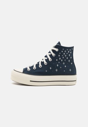 Zapatillas altas de lona en color navy, con patrones de estrellas blancas, cordones blancos y una puntera y suela de goma con una franja negra.