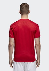 T-shirt sportivo rosso realizzato in tessuto leggero e traspirante; presenta maniche corte, colletto a girocollo e una texture liscia. Design semplice, senza fantasia.