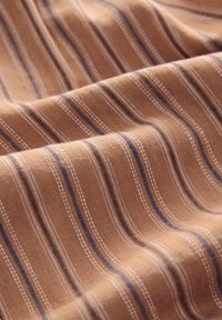 Tissu marron avec des rayures horizontales texturées en blanc, bleu et noir, présenté avec des plis doux et de légères ondulations.