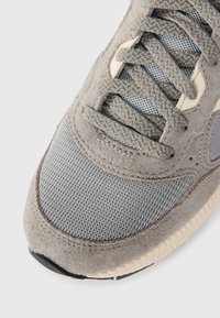 Sneakers grigi con una combinazione di materiali in suede e mesh, con una tomaia testurizzata, lacci prominenti e una suola imbottita.