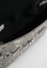 Harmaan tekstuurinen käsilaukun sisusta, jossa on musta vuori, vetoketjullinen tasku ja metallinen nepparikiinnitys. Sileä, tyylikäs materiaalipinta.