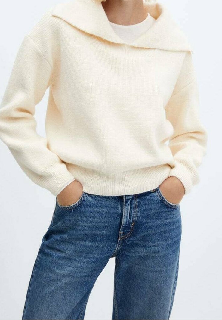 Pull en laine couleur crème avec un large col, des manches longues et des poignets côtelés, associé à un jean bleu taille haute. Design simple.