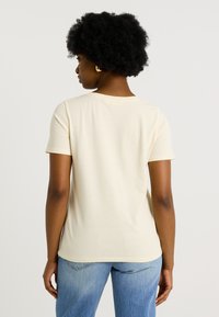 Camiseta de color crema de manga corta con cuello redondo, de tejido suave y corte relajado, combinada con unos vaqueros de color azul claro.