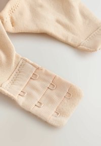 Béžová tkanina s hladkou textúrou, obsahujúca zapínanie na háčiky s tromi háčikmi, spevnené švy a mäkkú podložku.