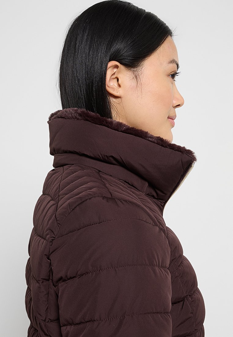 Veste en duvet bordeaux avec une texture côtelée, col haut doublé en fausse fourrure et motif matelassé. Fermeture éclair à l'avant.