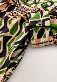 Mehrfarbiges Hemd mit einem lebendigen, abstrakten Muster in Grün, Schwarz und Braun. Baumwollstoff mit einem detailreichen, geknöpften Manschettenverschluss.