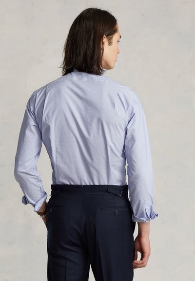 Lyseblå skjorte med lange ermer, knappkrage, buet kant og justerbare mansjetter, kombinert med mørke bukser med baklommer.