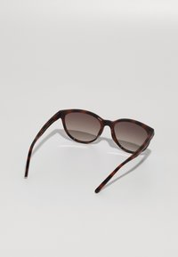Lunettes de soleil en acétate écaille de tortue brun, de forme ovale, avec des verres dégradés et des branches fines, présentant une finition lisse et brillante.