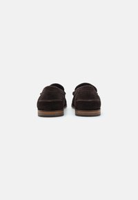 Mocassins en daim marron avec un bout arrondi, des coutures décoratives et une semelle contrastante de couleur marron clair. Pas de matériel ou d'accents visibles.