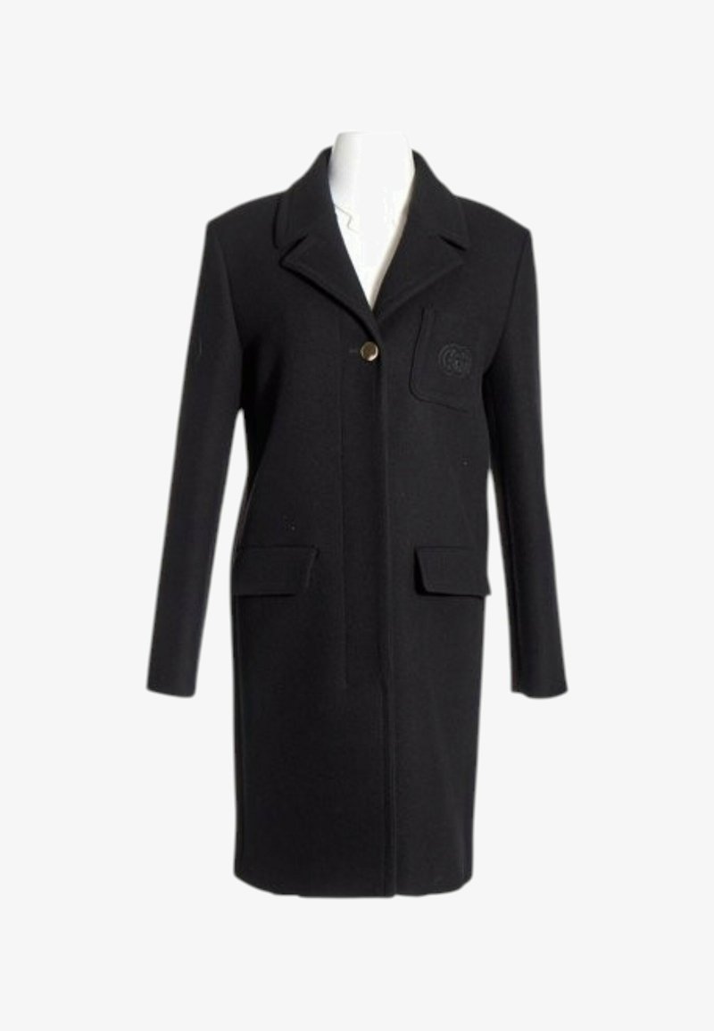 Long manteau noir avec fermeture à un bouton, col large à revers, deux poches à rabat à l’avant et une poche poitrine avec un écusson cousu.