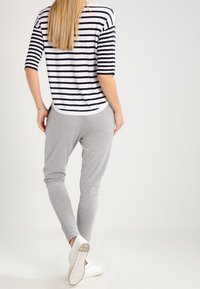 Outfit casual da donna con una maglietta a righe a maniche corte bianca e blu navy, abbinata a pantaloni grigi jogger e sneaker bianche.