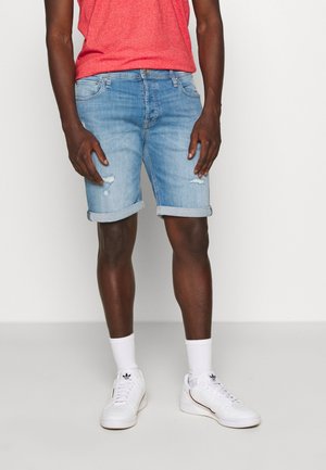 Pantalones cortos de mezclilla azul claro con dobladillos enrollados, con detalles desgastados. Se llevan con una camiseta roja y zapatillas blancas.