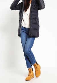 Gewatteerd jack met een donkergrijze romp en contrasterende mouwen, gecombineerd met een lichte trui, blauwe spijkerbroek en beige geïsoleerde laarzen met veters.