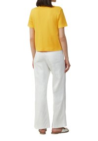 T-shirt jaune à manches courtes et cropped, associé à un pantalon blanc à jambes larges. Le tissu semble doux avec une texture lisse et un design simple.