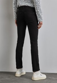 Svarta denimjeans med smal passform, detaljerad sömnad, fem fickor och en lätt urtvättad textur, parat med vita högskurna sneakers.