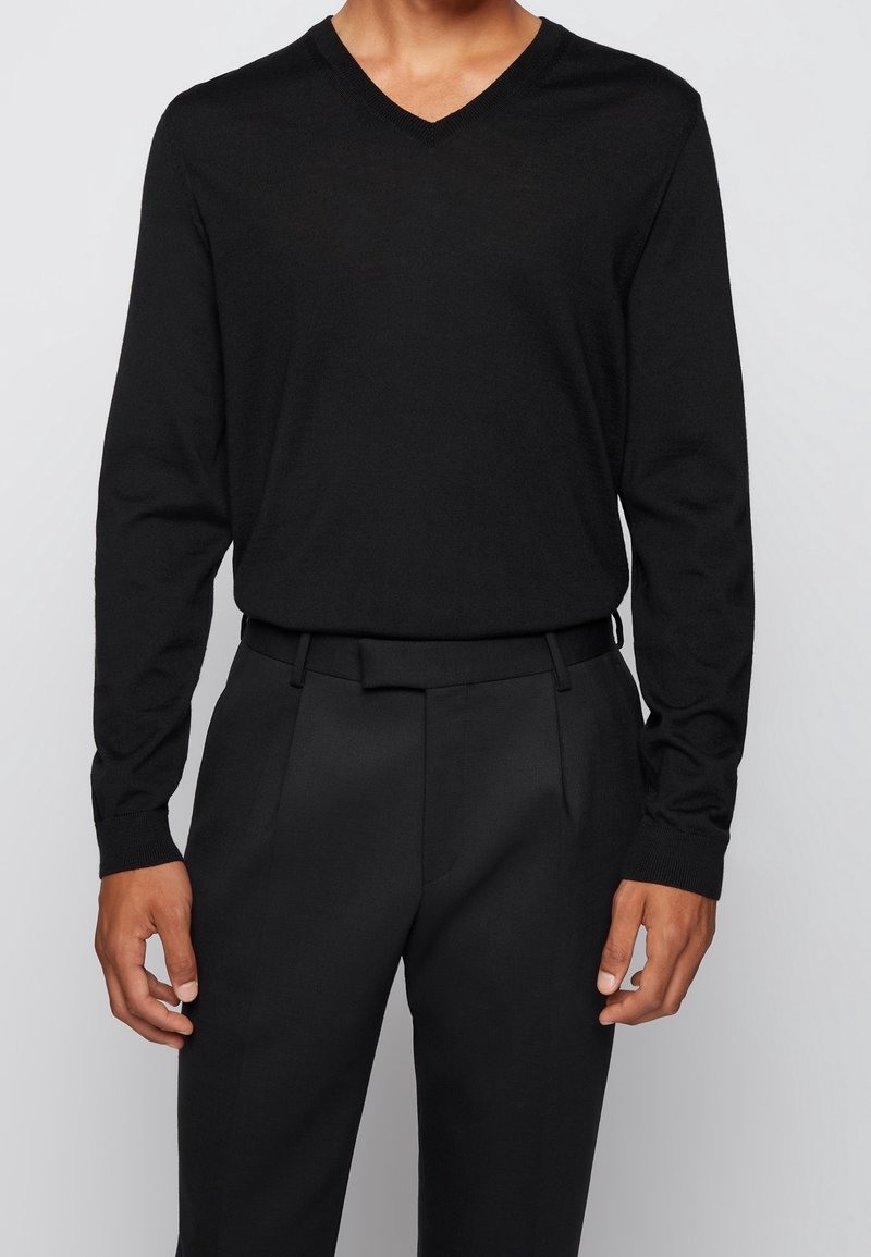 Černý dlouhý rukáv svetr s V-výstřihem, měkká textura, spárovaný s odpovídajícími černými kalhotami na míru; obojí má minimalistický design a čisté linie.