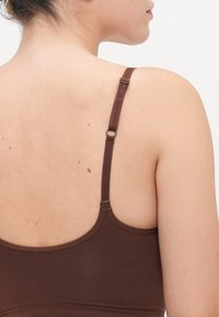 Sottocoperta marrone senza cuciture con spalline regolabili e una texture liscia. La parte posteriore presenta un design arrotondato e dettagli di cucitura minimi.