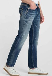 Jeans de mezclilla azul oscuro con un acabado descolorido, un leve desgaste y diseño de pierna recta. Cuenta con cinco bolsillos y detalles en bronce.