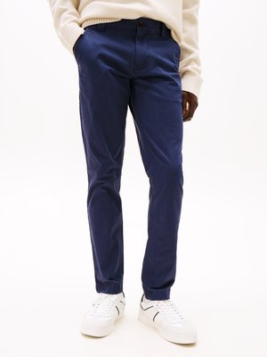 Navy blue cotton trousers with a relaxed fit, featuring front pockets, a button closure, and cuffed hems, paired with white sneakers.