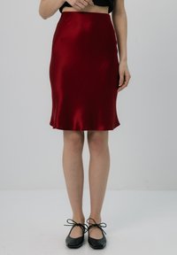 Czerwona satynowa spódnica midi o gładkiej fakturze, dopasowanym kroju i rozkloszowanym dole. Czarne baleriny z kokardkami dopełniają stylizację.