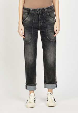 Schwarze Jeans aus Denim mit lockerem Schnitt, fünf Taschen, sichtbaren Nähten und aufgerollten Bündchen. Kombiniert mit weißen Sneakers.