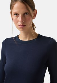 Granatowa koszula z długim rękawem i okrągłym dekoltem, wykonana z gładkiej tkaniny. Charakteryzuje się dopasowanym krojem i subtelnymi szwami na ramionach.