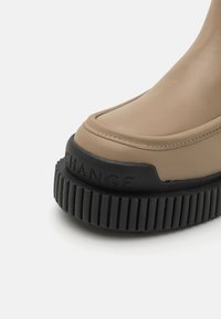Stivaletto sintetico beige alla caviglia con punta rotonda e suola in gomma nera strutturata. Presenta cuciture in rilievo e la scritta "CHANGE" impressa sulla suola.