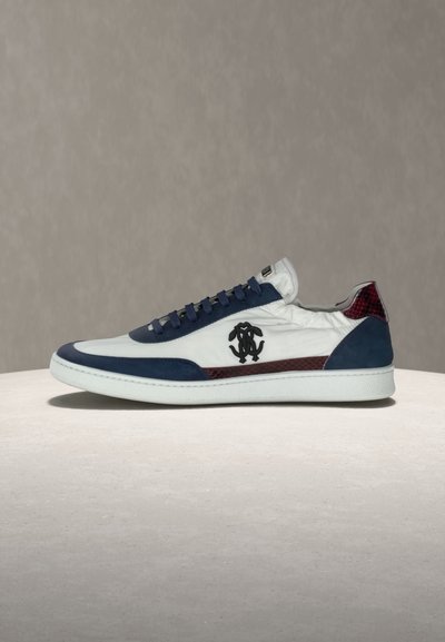 Baskets blanches avec accents bleu marine, garniture en cuir de serpent bordeaux, logo noir sur le côté et semelle blanche, exposées sur une surface claire.