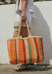 Sac en toile tissé avec des rayures orange, vertes et rouges, fabriqué en fibres naturelles. Il dispose de deux poignées solides pour un transport facile.