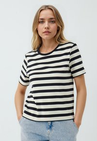 T-shirt a righe con strisce orizzontali nere e off-white, maniche corte, colletto a girocollo e vestibilità comoda. Abbinato a jeans in denim chiaro.