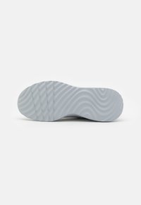 Sole of a sneaker, featuring a wavy textured pattern, made of light gray rubber, with defined traction grooves and a rounded toe shape.