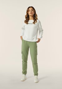 Sweatshirt blanc avec texte imprimé, associé à un pantalon cargo vert avec poches latérales et poignets élastiques, complété par des baskets blanches.