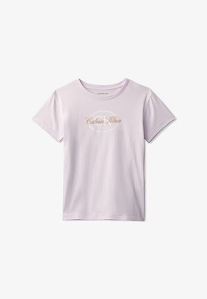 Dziewczyna w jasnofioletowej koszulce Calvin Klein i szerokich niebieskich dżinsach, trzymająca jasną kurtkę jeansową w lewej ręce.