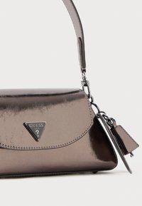Sac à main gris métallisé avec une forme structurée, accent en triangle logo, bandoulière amovible et petit détail de tag attaché. Fini lisse et brillant.