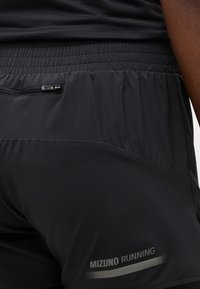 Gros plan sur un short de course noir avec taille élastique, poche arrière zippée et logo "Mizuno Running" près de l'ourlet.