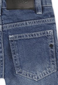 Jeans in denim blu con una finitura testurizzata. Presentano una tasca posteriore, dettagli in cucitura e un'etichetta in pelle nera del marchio in vita.