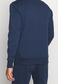 Sweat-shirt bleu marine avec un col rond, des manches longues, des poignets et un ourlet côtelés, fabriqué dans un tissu doux et texturé, au design simple.