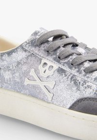 Srebrne sneakersy z teksturą, z szarymi sznurówkami, z białym logo czaszki i skrzyżowanych kości po boku. Biała gumowa podeszwa.