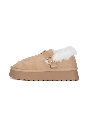 Scarpa beige in pelle scamosciata slip-on con suola spessa in gomma, cinturino regolabile con fibbia dorata e fodera bianca soffice intorno al colletto del tallone.
