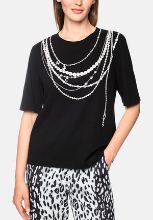 Woman wearing a black short-sleeve top with white printed layered pearl necklace design and black and white animal print pants.