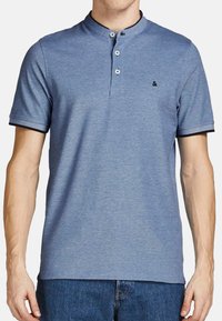 Blauwe polo met korte mouwen, hoge kraag, placket met drie knopen, contrasterende halslijn en zwarte afwerking op de mouwen. Zachte stofstructuur.