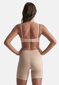 Beige naadloze beha met verstelbare bandjes en haaksluiting, gecombineerd met bijpassende shorts tot halverwege de dijen, beide gemaakt van een gladde, rekbare stof.