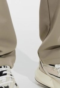 Bermuda tapered berwarna krim dipadukan dengan sepatu sneaker chunky, menampilkan campuran aksen krem muda dan hitam, dengan tali yang tekstur dan detail sol.