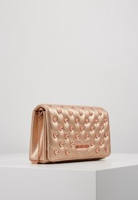 Vadderad metallisk rose gold handväska med hjärtformade nitar, kedjestropp och logodetalj på framsidan. Slät yta och rektangulär form.
